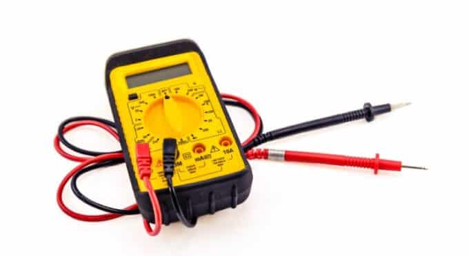 um voltímetro amarelo com fios preto e vermelho no fundo branco