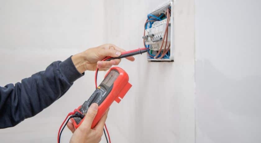 Uma foto de uma mão segurando um voltímetro e a outra segurando uma espécie de chave conectora na parede