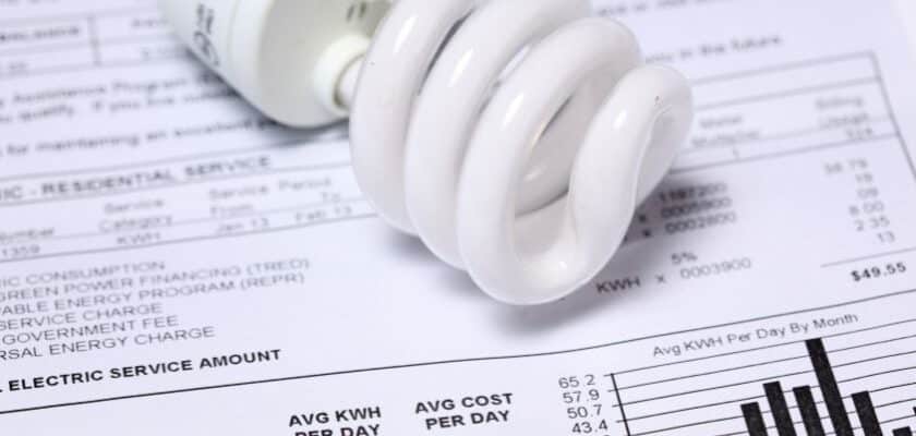 Uma lâmpada fluorescente compacta (LFC), de cor branca e formato espiralado, colocada sobre uma conta de luz detalhada.