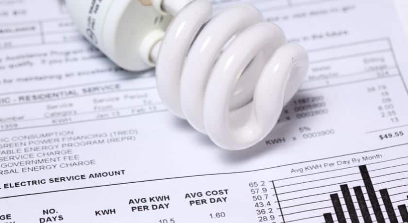 Uma lâmpada fluorescente compacta (LFC), de cor branca e formato espiralado, colocada sobre uma conta de luz detalhada.