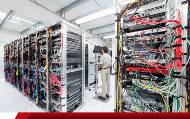 Técnico trabalhando em corredor de data center cheio de cabos e servidores.