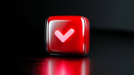 A imagem é um close-up digital 3D de um ícone de marca de seleção (check mark). O ícone está dentro de um cubo com cantos arredondados, de cor vermelha vibrante e brilhante, com um acabamento que lembra vidro ou gel. A marca de seleção em si é um V grande e suave, de cor rosa pálido ou vermelho claro, centralizado no cubo. O fundo é preto sólido, e a forte iluminação de cima cria um reflexo vermelho intenso na superfície escura sobre a qual o cubo está apoiado.