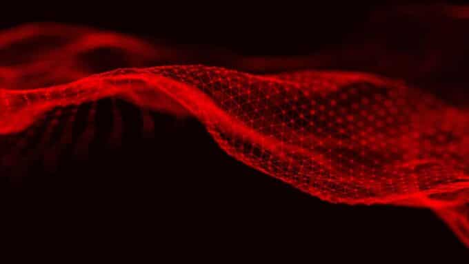 Uma representação digital abstrata em tons de vermelho e preto. Linhas e pontos luminosos formam uma malha tridimensional que se assemelha a uma onda ou rede em movimento, transmitindo uma sensação de energia e fluxo de dados.