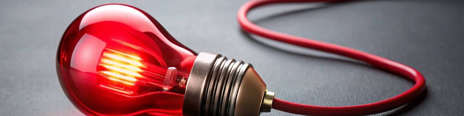 Lâmpada Vermelha Acesa Esta é uma imagem de close-up e de estúdio de uma lâmpada incandescente ou LED com bulbo de vidro vermelho, deitada de lado sobre uma superfície escura (possivelmente preta ou cinza escuro).