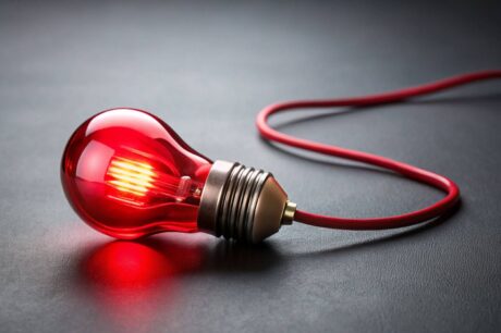 Lâmpada Vermelha Acesa Esta é uma imagem de close-up e de estúdio de uma lâmpada incandescente ou LED com bulbo de vidro vermelho, deitada de lado sobre uma superfície escura (possivelmente preta ou cinza escuro).