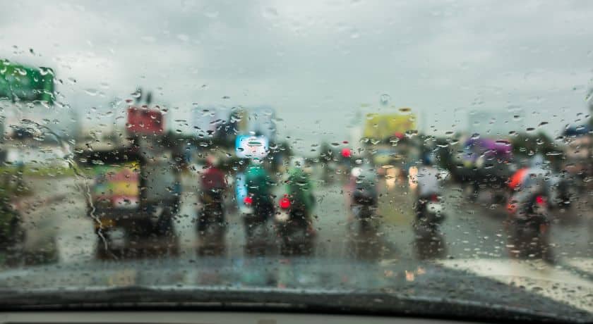Chuva forte no para-brisa de um carro, mostrando o trânsito congestionado com motocicletas e veículos na rua.