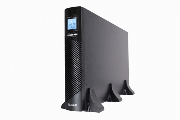 No-break preto da marca TS Shara em posição vertical, com formato retangular e apoio na base. Na parte frontal há uma grade de ventilação, um visor digital azul exibindo informações elétricas e botões de controle logo abaixo do display. Fundo branco.