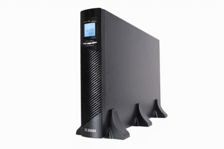 No-break preto da marca TS Shara em posição vertical, com formato retangular e apoio na base. Na parte frontal há uma grade de ventilação, um visor digital azul exibindo informações elétricas e botões de controle logo abaixo do display. Fundo branco.