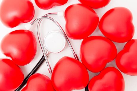 Conjunto de corações vermelhos dispostos sobre um fundo claro, com um estetoscópio metálico posicionado ao centro. A imagem remete a cuidados, monitoramento e saúde, simbolizando proteção, confiabilidade e atenção constante.