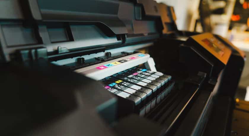 Visão interna detalhada de uma impressora plotter profissional, exibindo os cartuchos de tinta colorida (CMYK) alinhados.