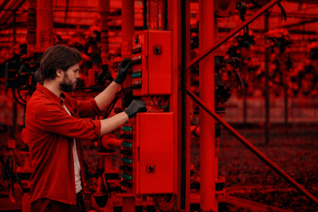 Homem usando luvas trabalha em um painel de controle elétrico em ambiente industrial.