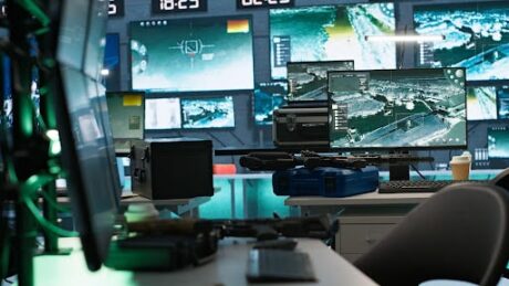 Sala de monitoramento com telas exibindo câmeras de segurança e equipamentos eletrônicos.