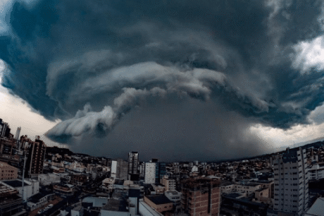 Nuvens escuras e densas formam uma tempestade intensa sobre uma cidade, cobrindo prédios e deixando o céu ameaçador.