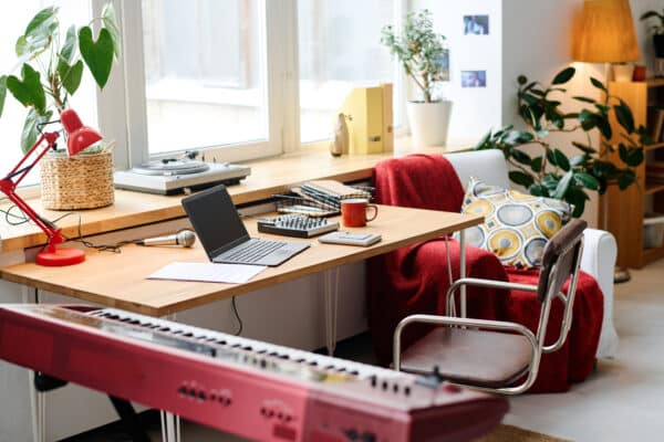 Home office com mesa, notebook e equipamentos de áudio em ambiente confortável e iluminado.