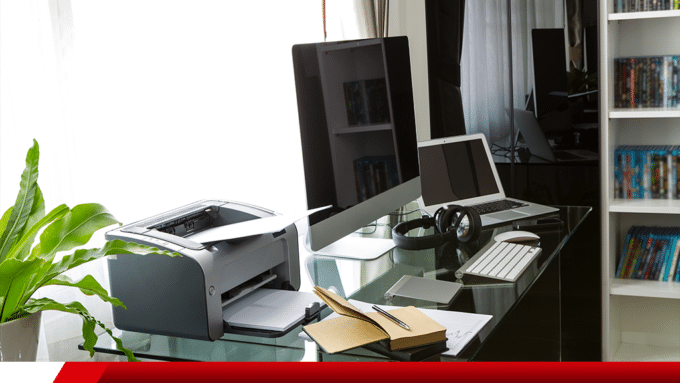 Mesa de trabalho com computador, notebook, impressora e acessórios de escritório.