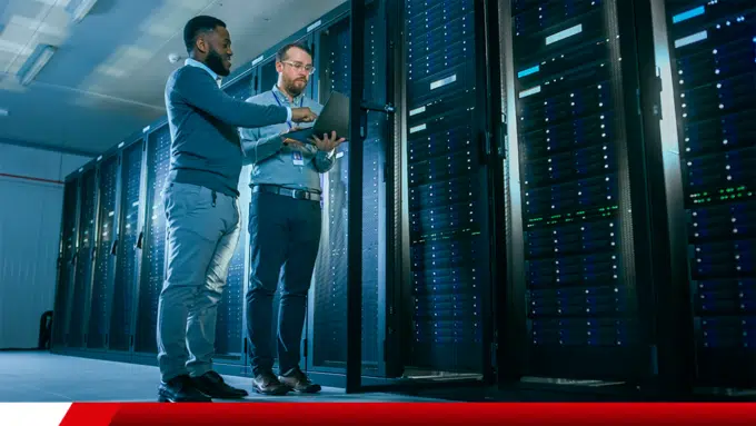 Dois profissionais analisam equipamentos em data center com racks de servidores.