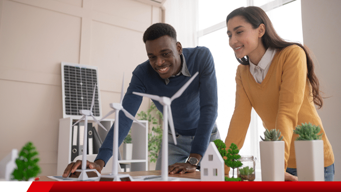 Dois profissionais analisam maquetes de energia renovável com turbinas e painel solar.