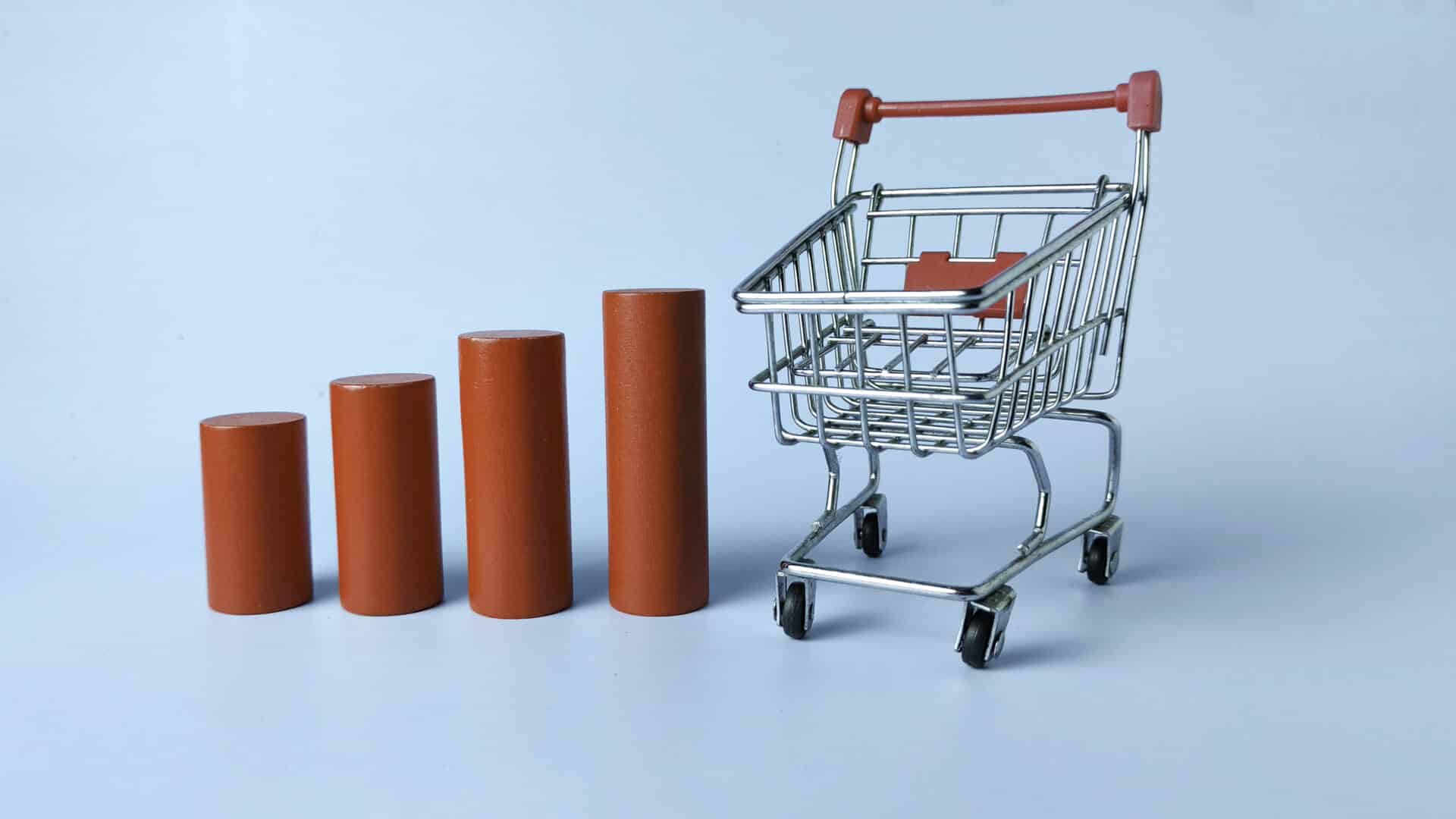 Carrinho de compras ao lado de quatro barras vermelhas em crescimento, representando aumento nas vendas e no consumo.