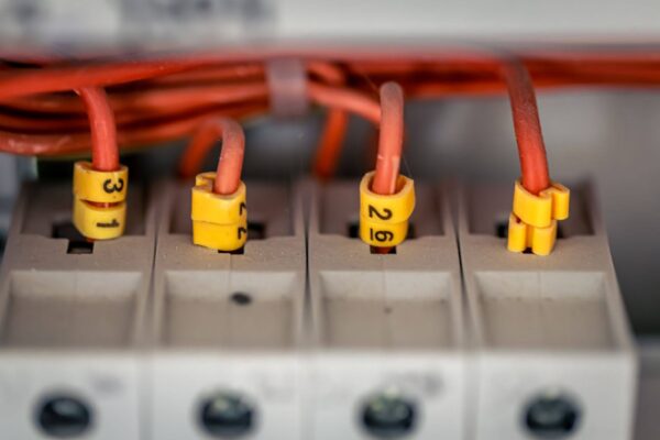 Close-up de uma instalação elétrica com vários cabos vermelhos conectados a terminais numerados em um painel, destacando detalhes da fiação e das conexões elétricas.